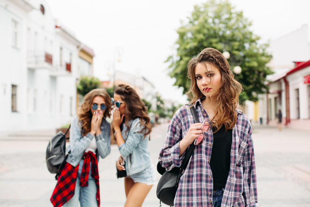 portrait sad beautiful teen girl checked shirt with braids looking camera against two friends sunglasses denim clothes gossiping about her street unfocused
