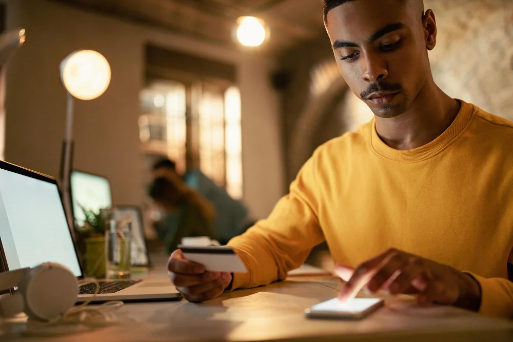 african american businessman using credit cart mobile phone while checking his online bank account during late night work office